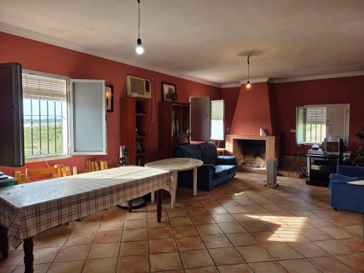 Salón amplio con paredes rojas, mesa, sillones y chimenea, iluminado por luz natural.